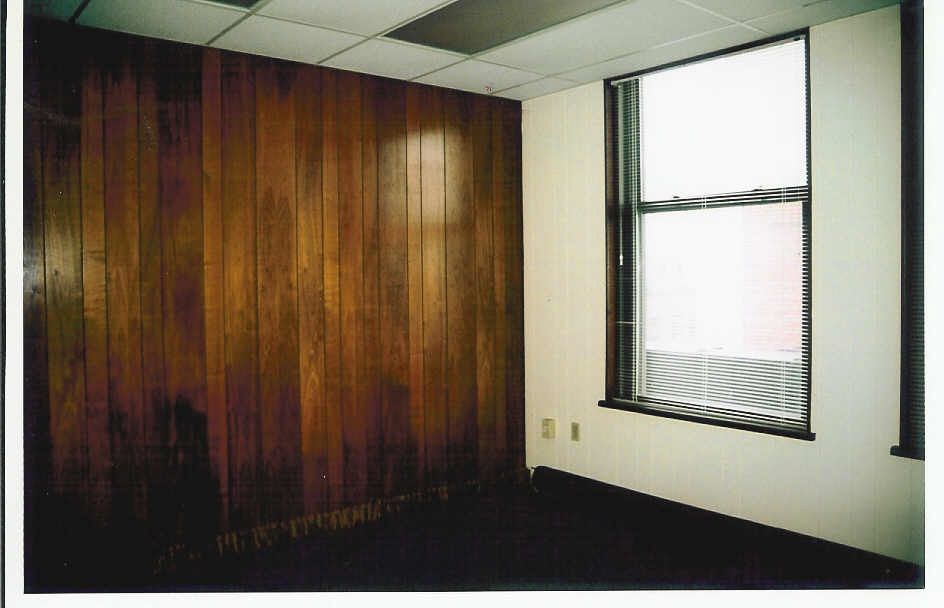 Original office with dark wood paneling, blinds, and a dropped acoustic ceiling.