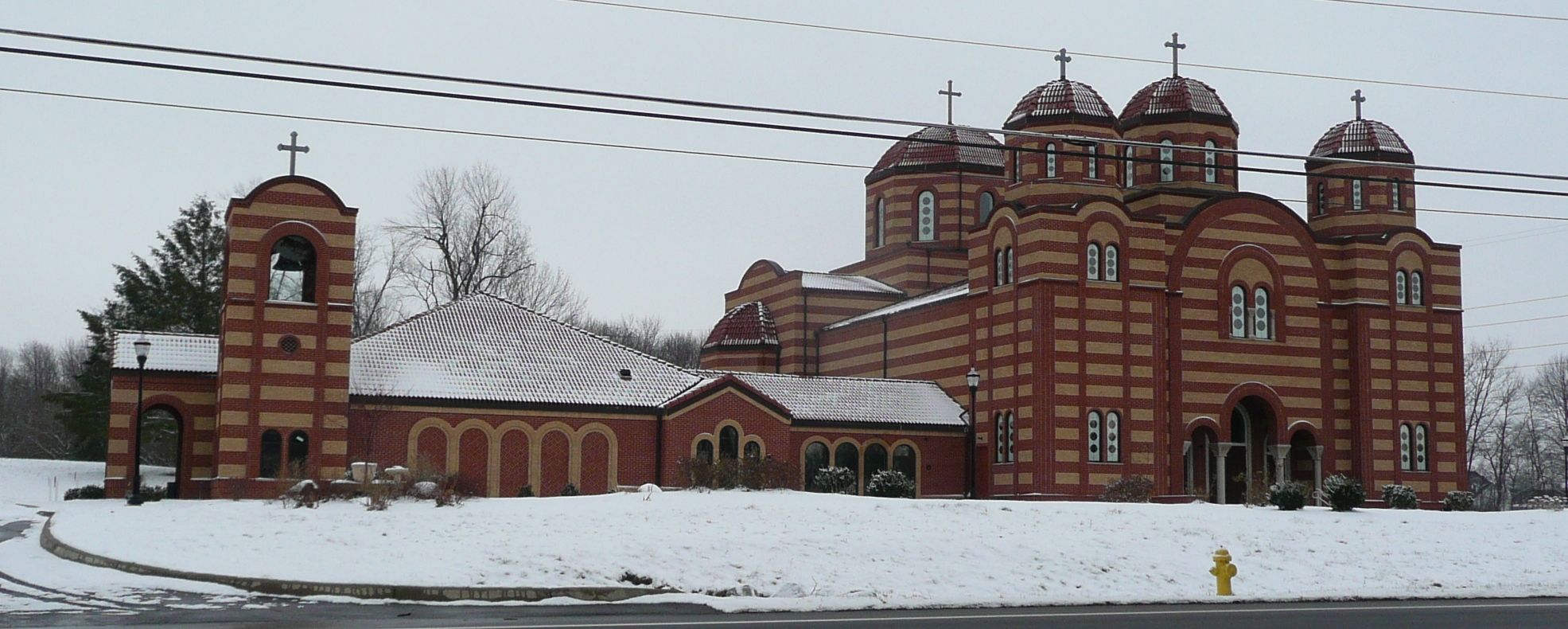 Red and tan striped brick Byzantine-style church with domed towers and bell tower in winter snow.